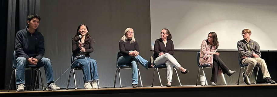 Group of students and staff members sitting on a stage for a panel discussion.
