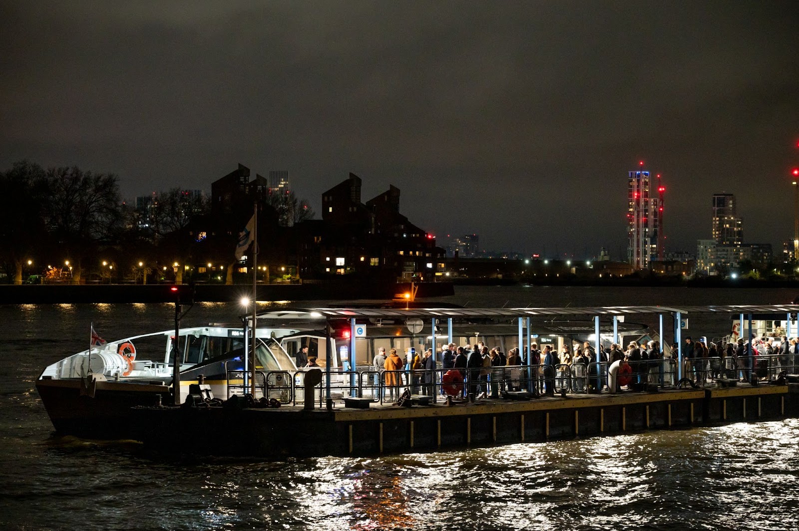 Uber Boat gliding along the Thames River at night, with iconic landmarks like Tower Bridge illuminated in the background