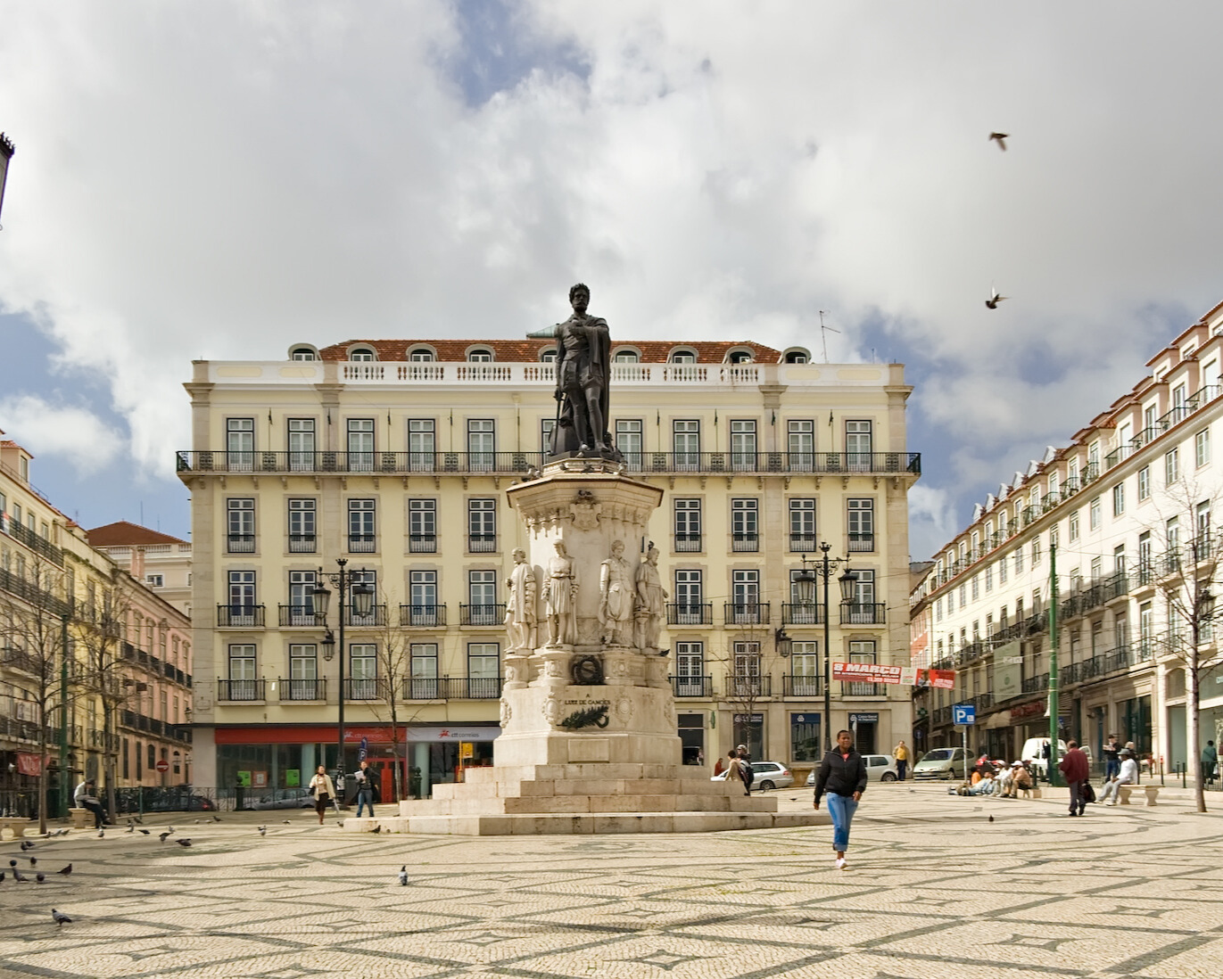 A statue in the center with a mix of historic and modern buildings around it.