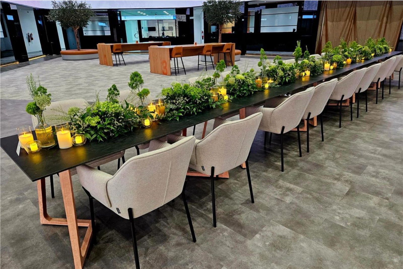 Spacious event venue with a long dining table, neutral chairs, and greenery centrepieces for corporate or private events.