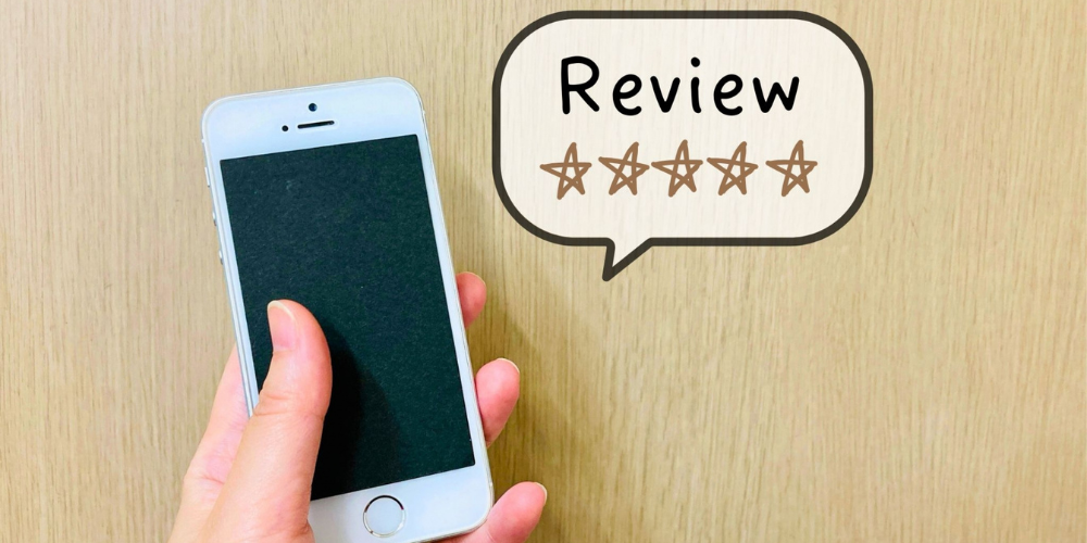 木目の背景にスマートフォンを持つ手と「Review ★★★★★」の吹き出し