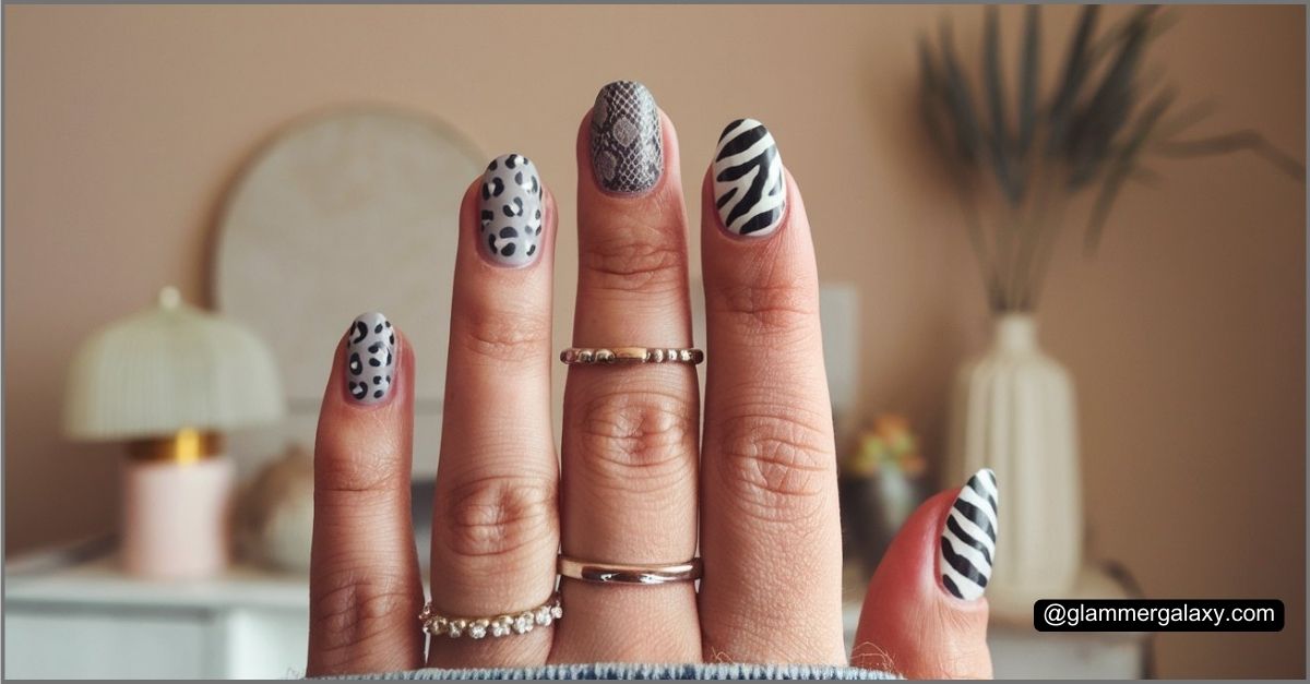 Hand displaying nails with black and white animal print designs against a blurred room background.