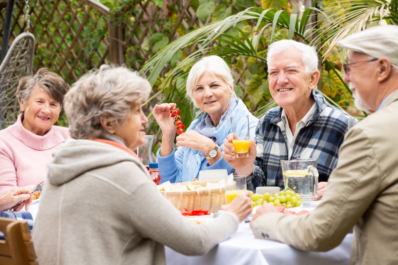 A group of happy older adults sit outside while dining together.