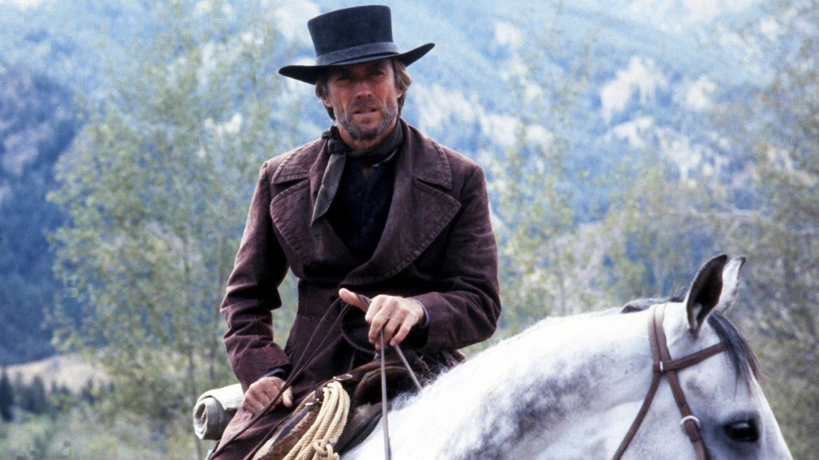 Clint Eastwood montando un caballo gris, con atuendo de vaquero oscuro y un sombrero negro, capturado en una escena de la película 'Pale Rider'.