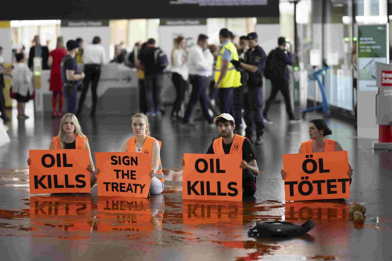 Four activists kneel on the oil strewn floor of an airport terminal with Oil Kills signs