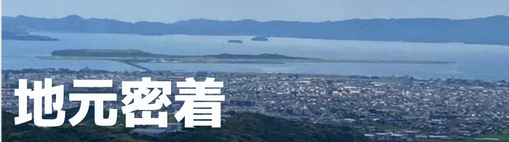 大村湾と市街地を見下ろすパノラマ写真に、大きく「地元密着」と白文字で重ねたバナー