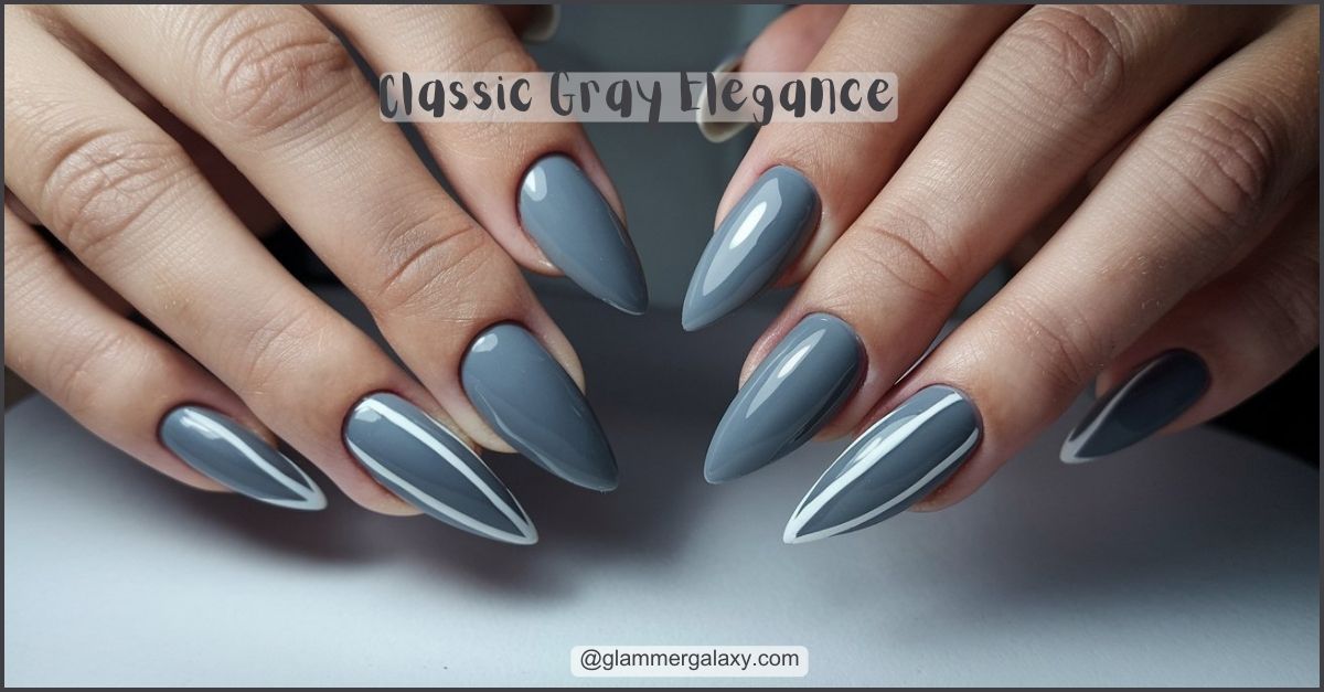 Long, gray, stiletto nails with white accents displayed on hands against a neutral background.