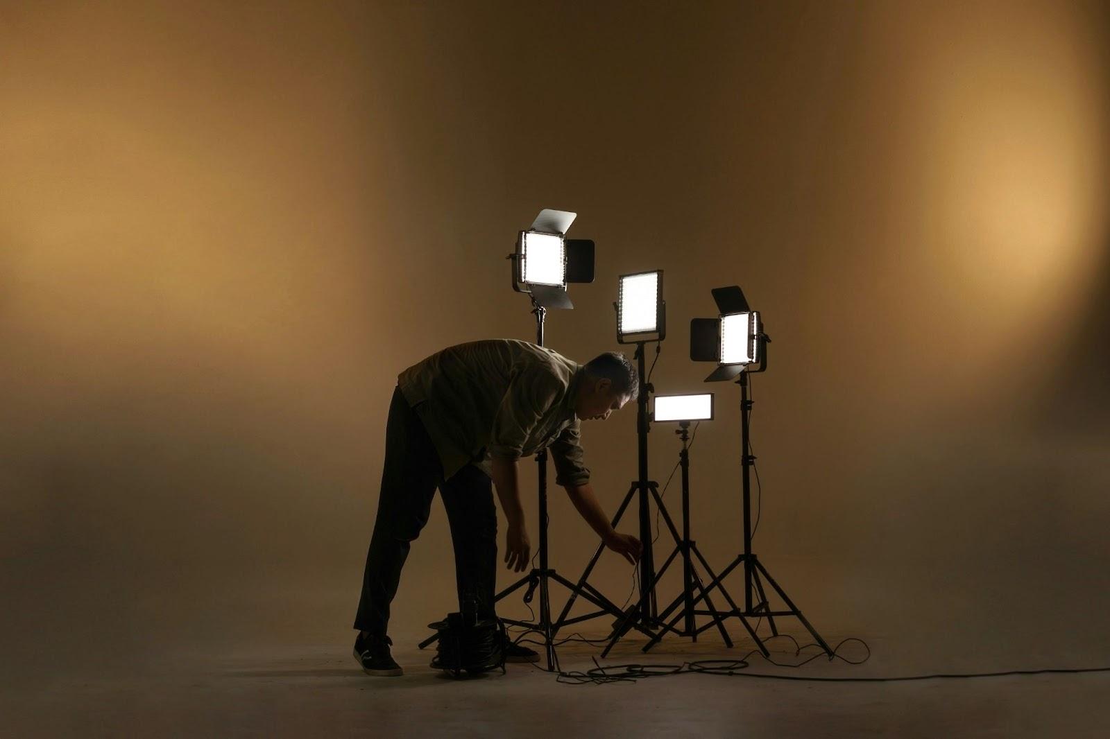 An engineer bending down to adjust LED panels on a set.