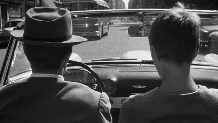 Silhouette of a man driving a convertible with a short-haired woman seated next to him.