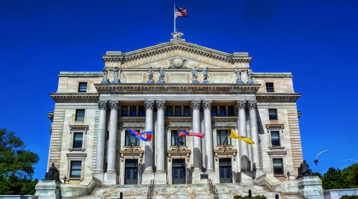 (Historic courthouse building with grand pillars, statues, and waving flags under a clear blue sky—symbolizing justice, law, and civic authority.)