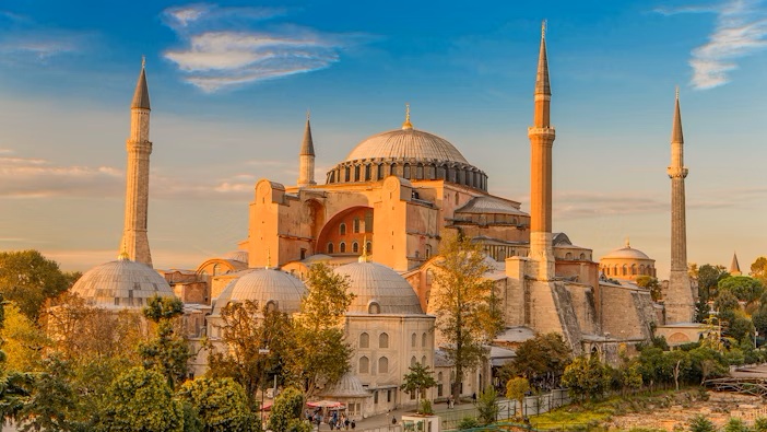 Sunset view of Hagia Sophia Grand Mosque in Istanbul, Turkey, featuring historic Byzantine architecture, large central dome, and surrounding minarets with a golden sky backdrop