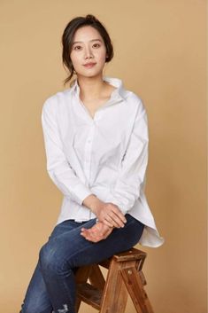 This contains an image of Kim Mi-soo  sitting on top of a wooden stool wearing a white shirt and blue jeans