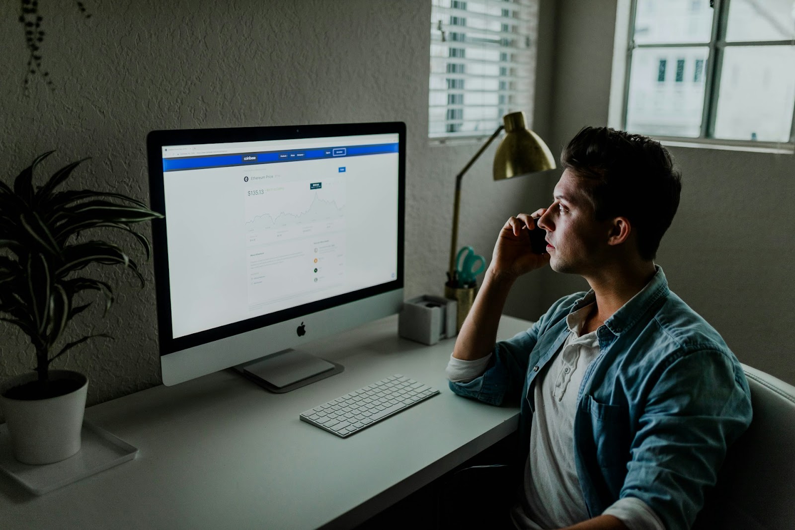 A man sitting at a desk, focused on his computer screen while browsing talking someone from the phone