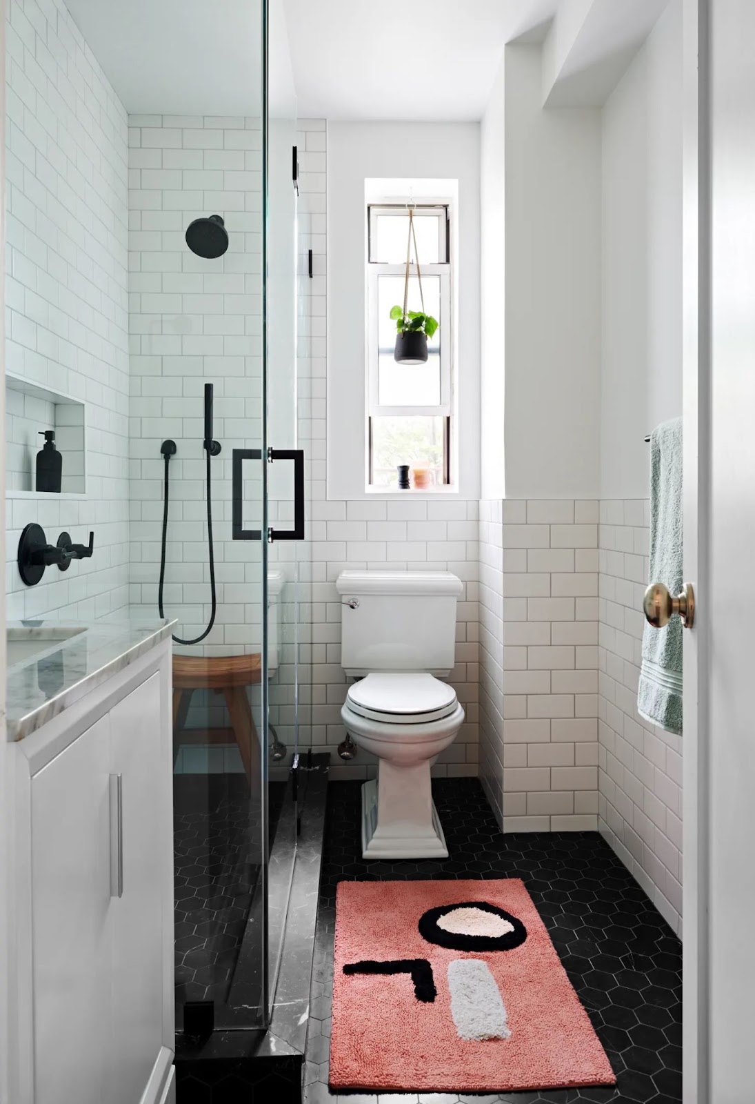 Small bathroom with glass framed walk-in shower, white subway tile walls, black hexagonal flooring, and a white vanity