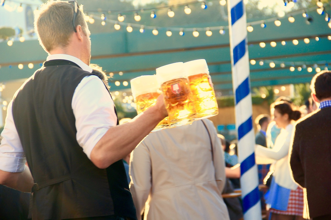 A bartender carries three jugs of craft beer and walks his way through a crowd.