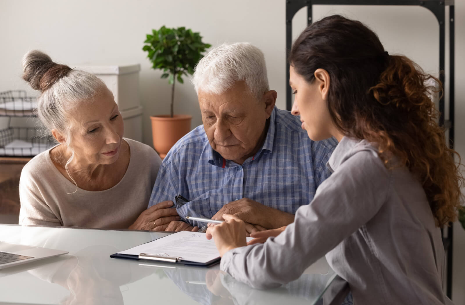 A senior reads a legal document for power of attorney before signing while his wife and adult daughter explain what it means.