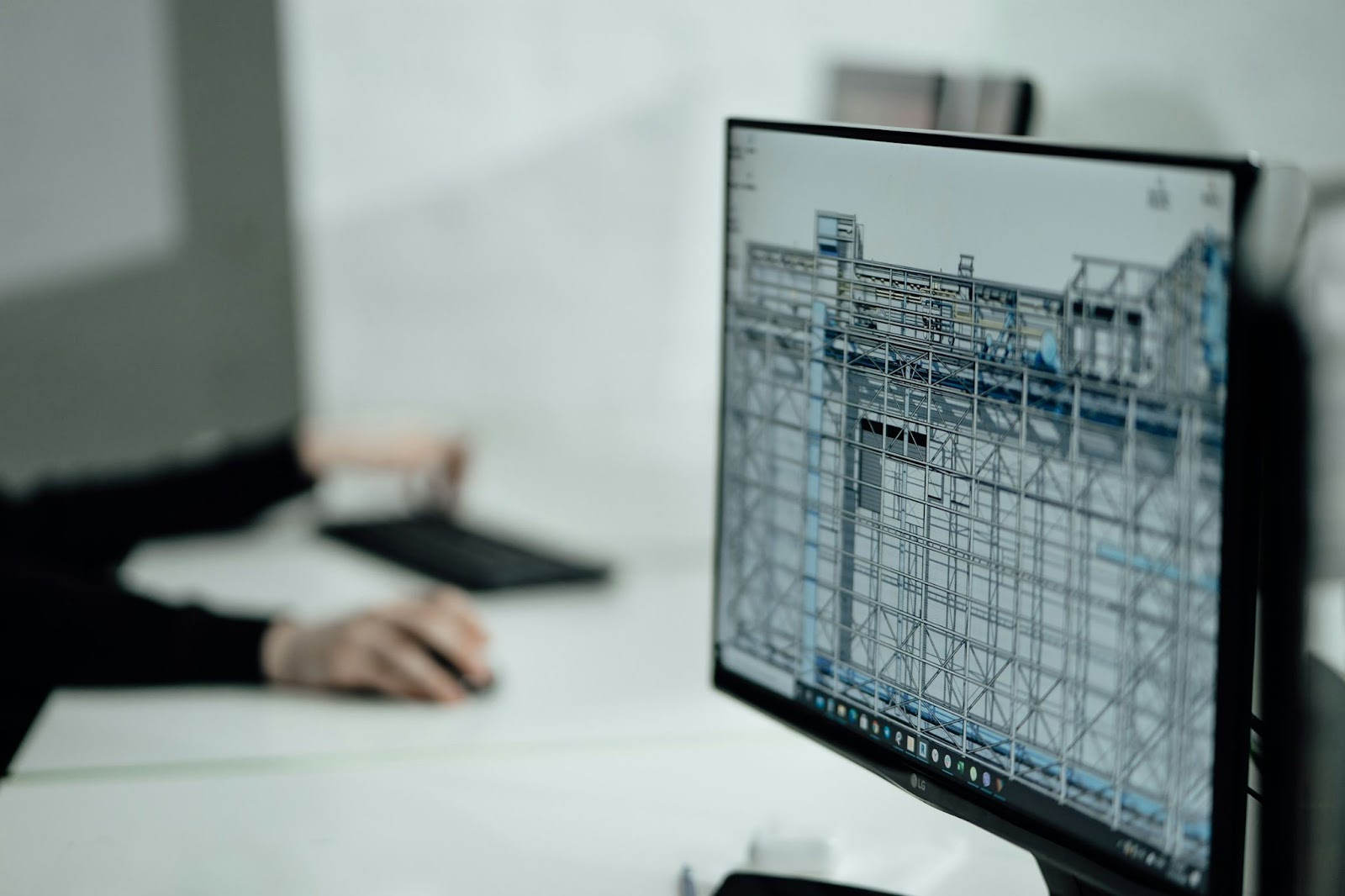 A person works at a desk with a computer screen displaying a detailed architectural design, emphasizing BIM 3D Design.