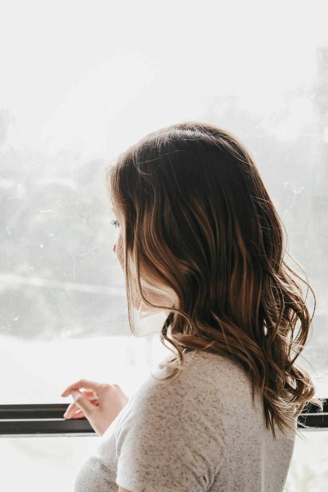 Woman looking out window with softly curled clip-in hair extensions