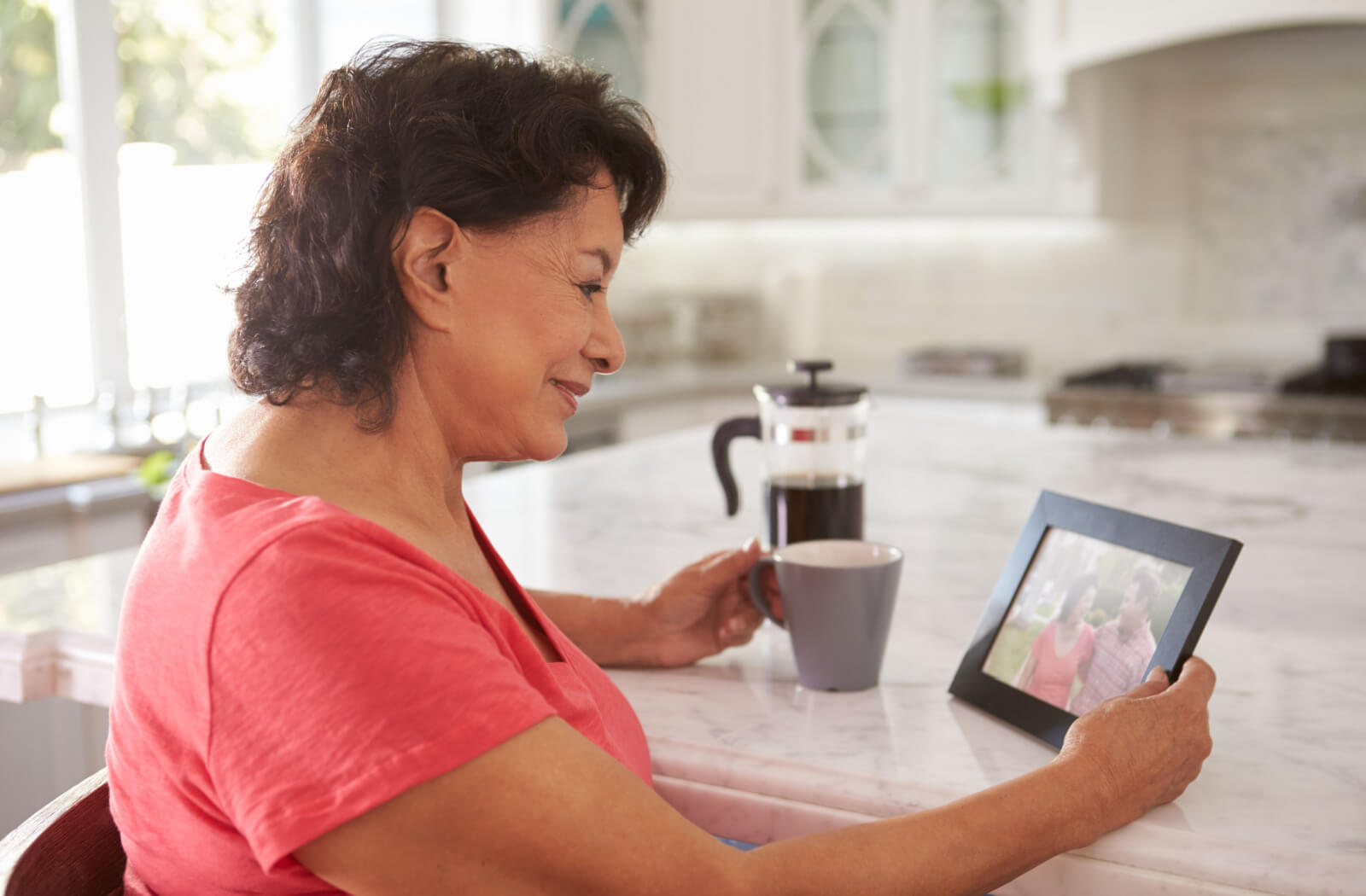 An older adult woman looking fondly at a photo in her kitchen.