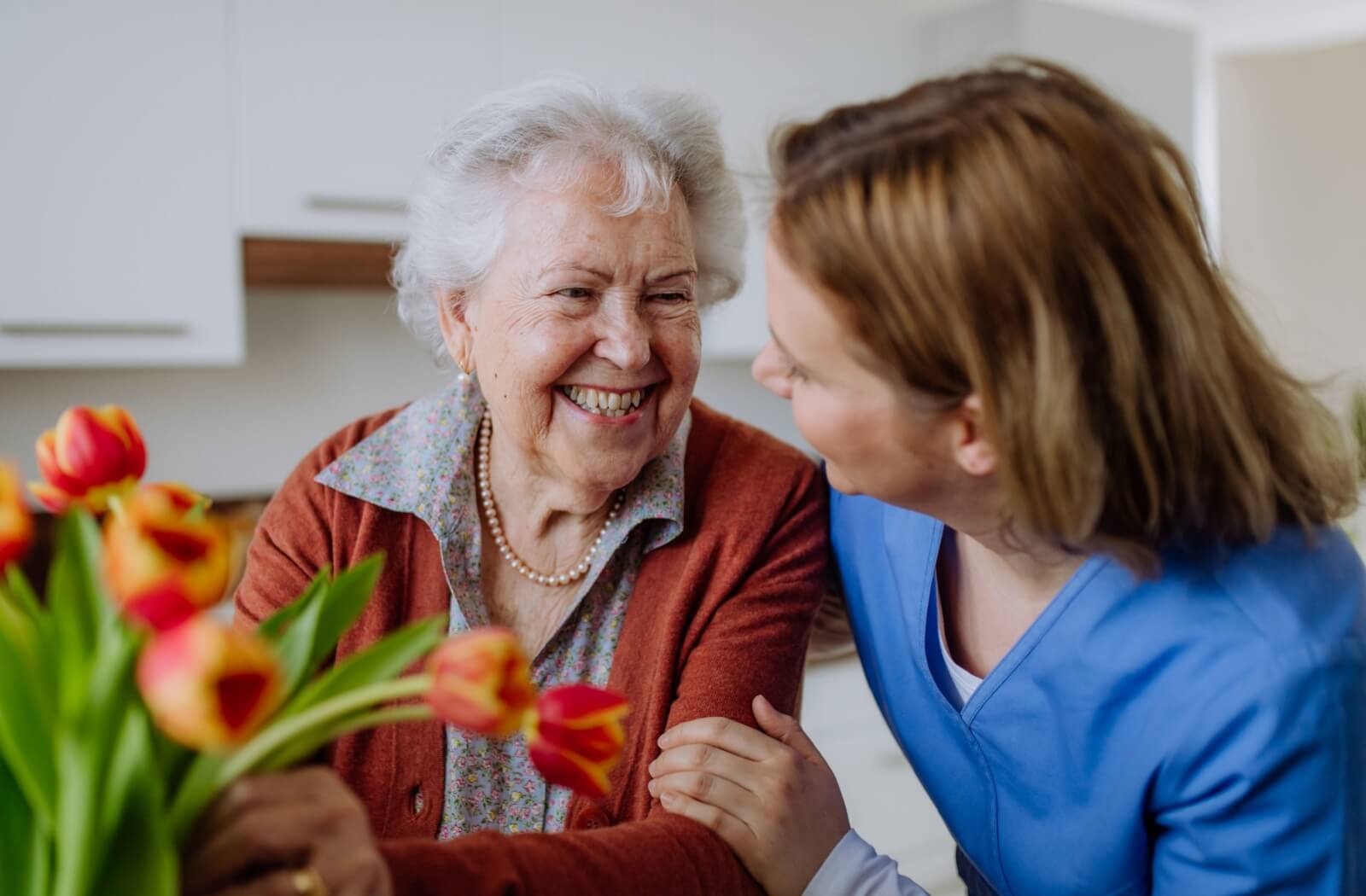 A staff member and older adult smiling while putting tulips in a vase.