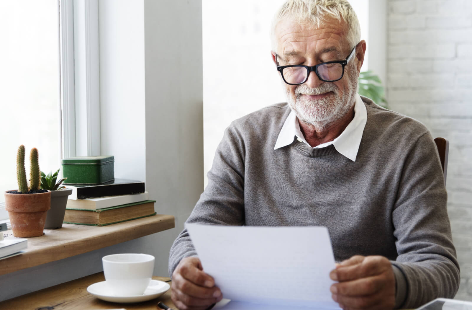 An older adult smiling while checking his trivia answers on a sheet of paper while enjoying his morning coffee.
