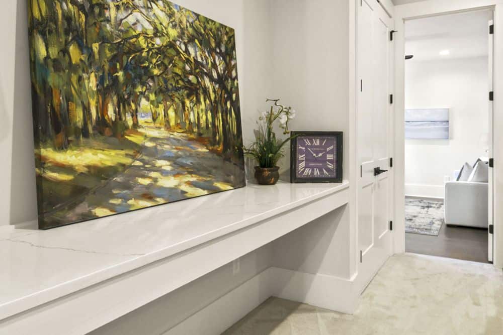 Hallway with built-in cabinets and table topped with a large painting and clock.