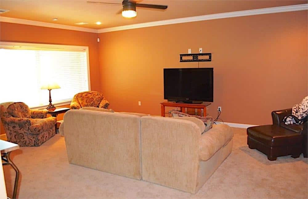 The game room is filled with patterned armchairs, a beige sofa, a leather lounge chair, and a TV sitting on a wooden stand.