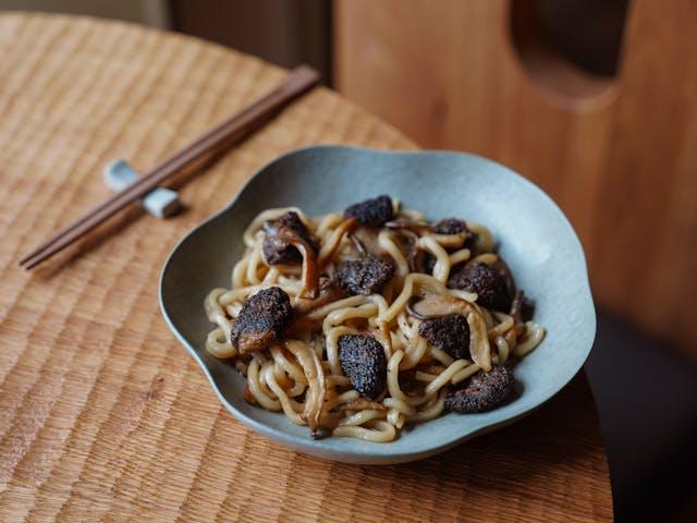 A bowl of noodles with mushrooms

Description automatically generated