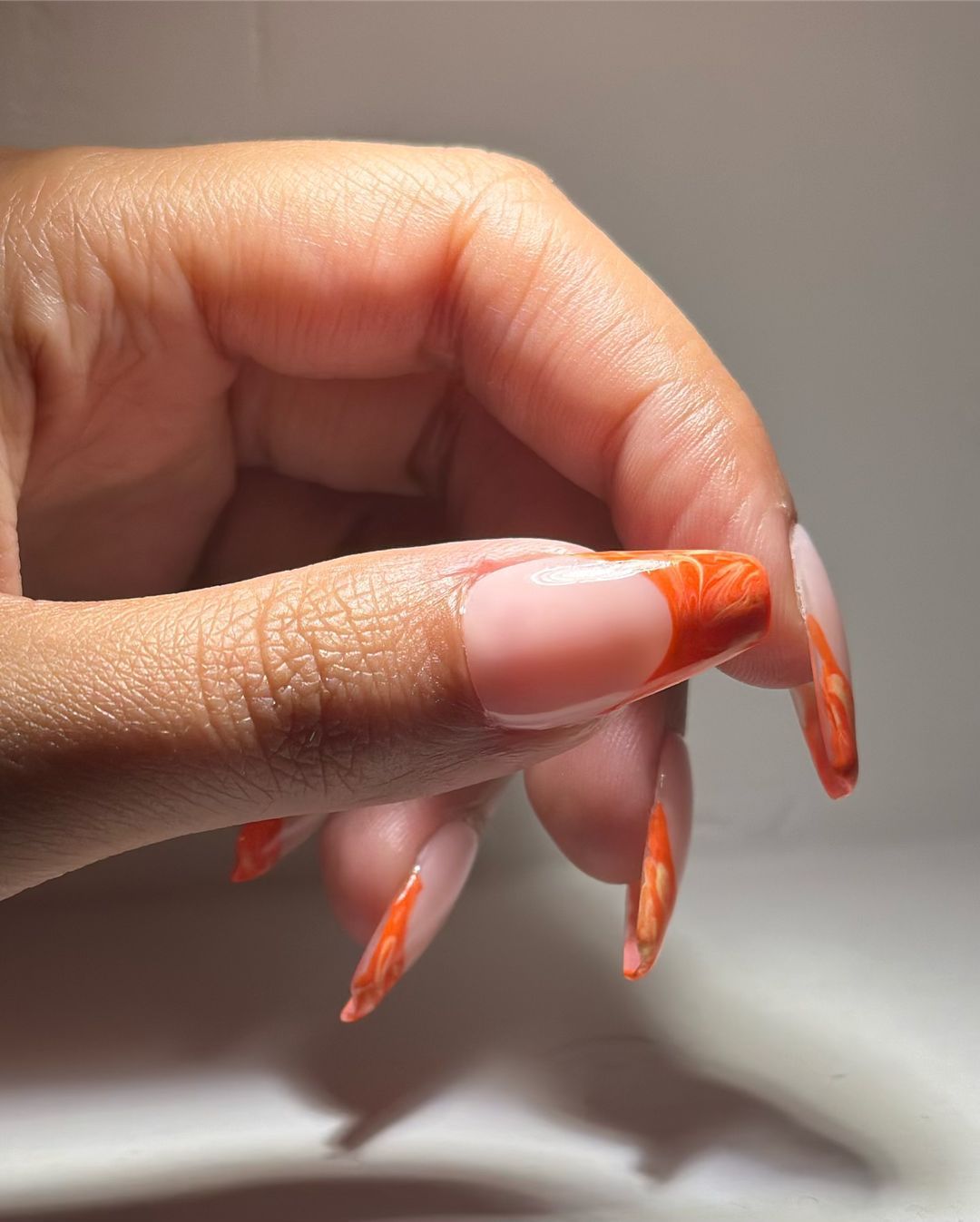 Close up of nails with glittery orange nails having Swirly Orange French Design