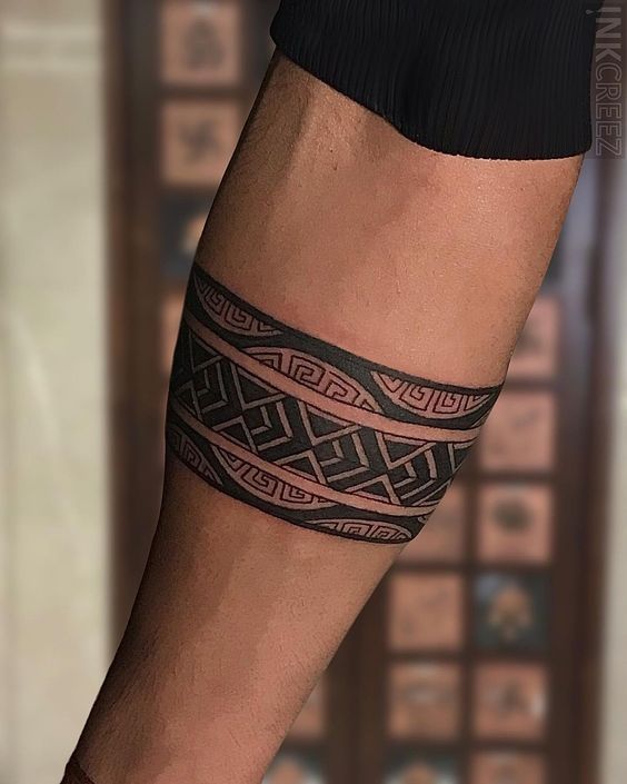 Arm with intricate black geometric band tattoo, featuring tribal patterns, symbolic designs and cultural artistry.