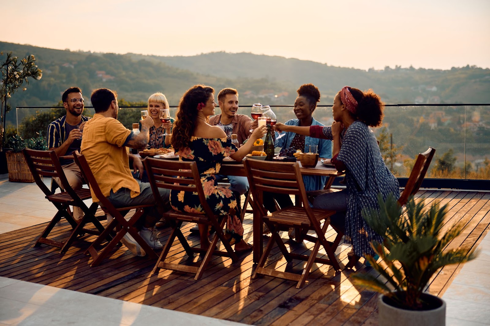 A diverse group of friends click glasses before drinking wine on a deck. 