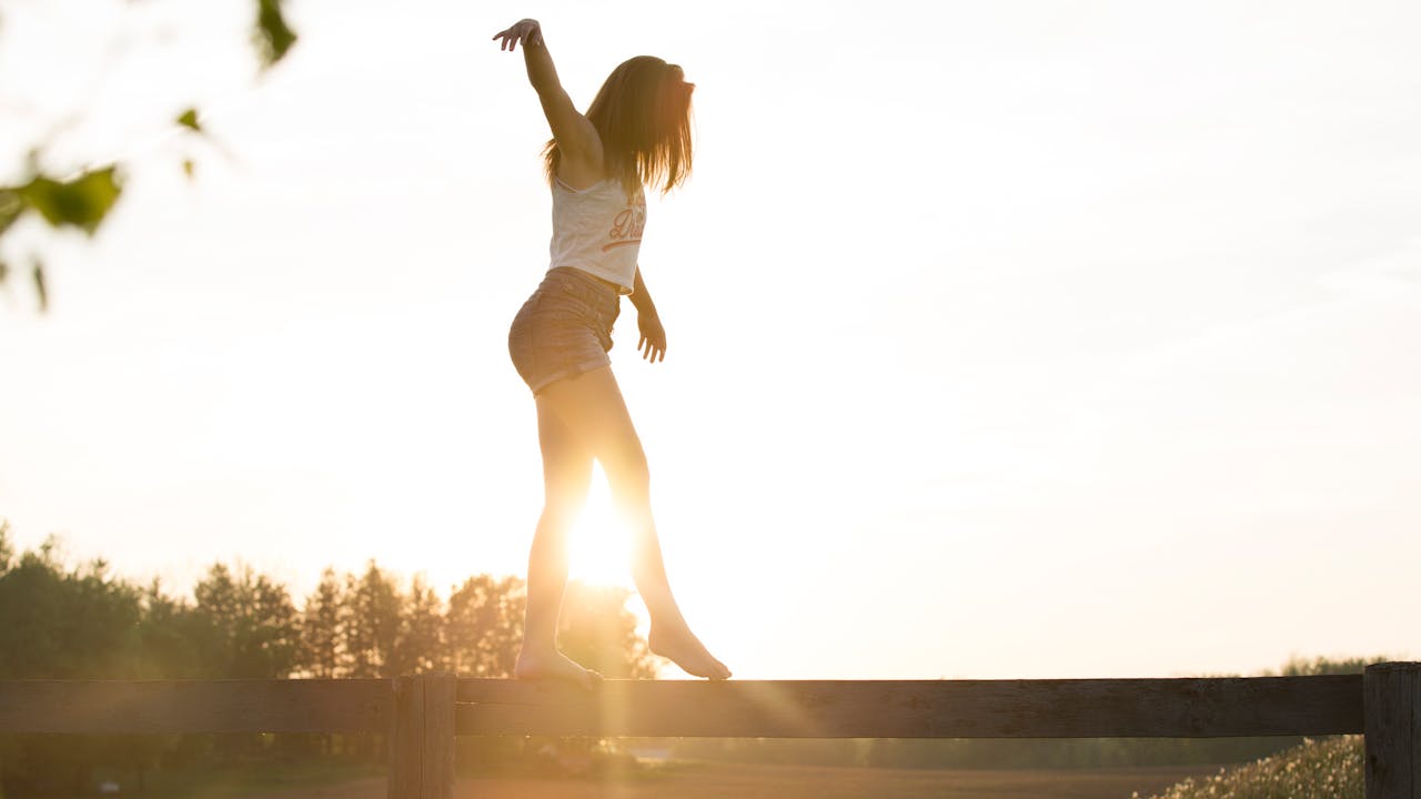 A woman stands on a fence, arms wide open, embracing the moment.