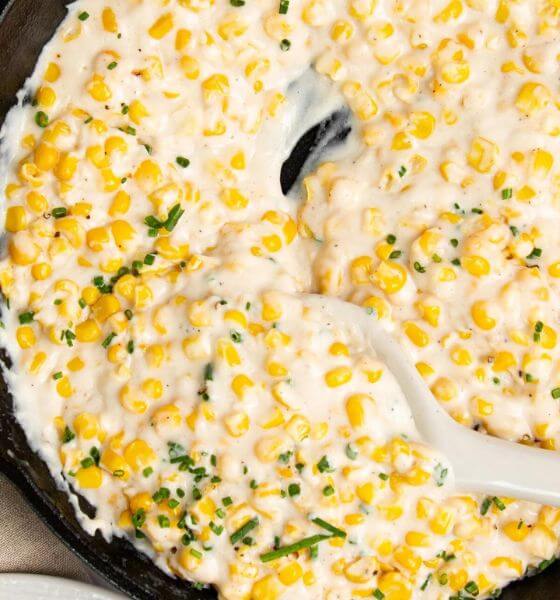 Creamed corn in black skillet with white serving spoon