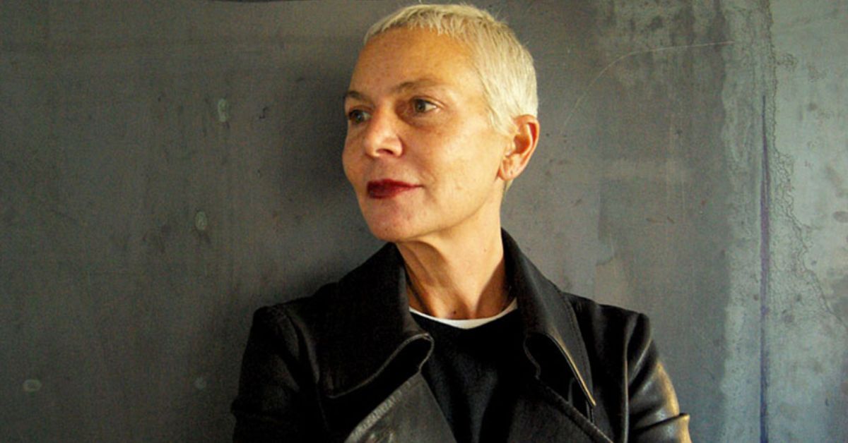 A woman with a buzz cut, featuring short white hair, wearing a stylish black jacket, exuding confidence and elegance.