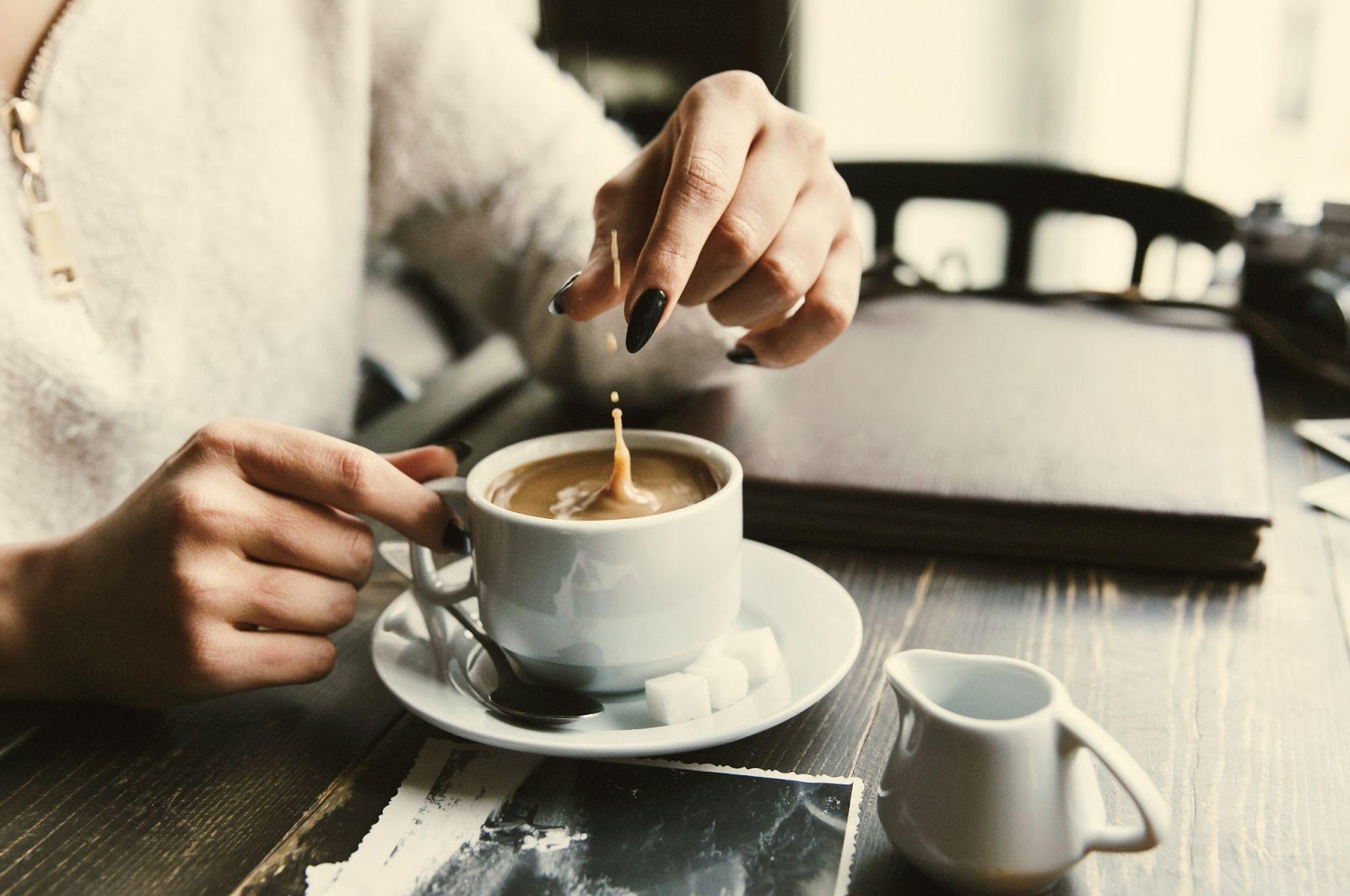 A woman prepares to stir a cup of coffee with a spoon.