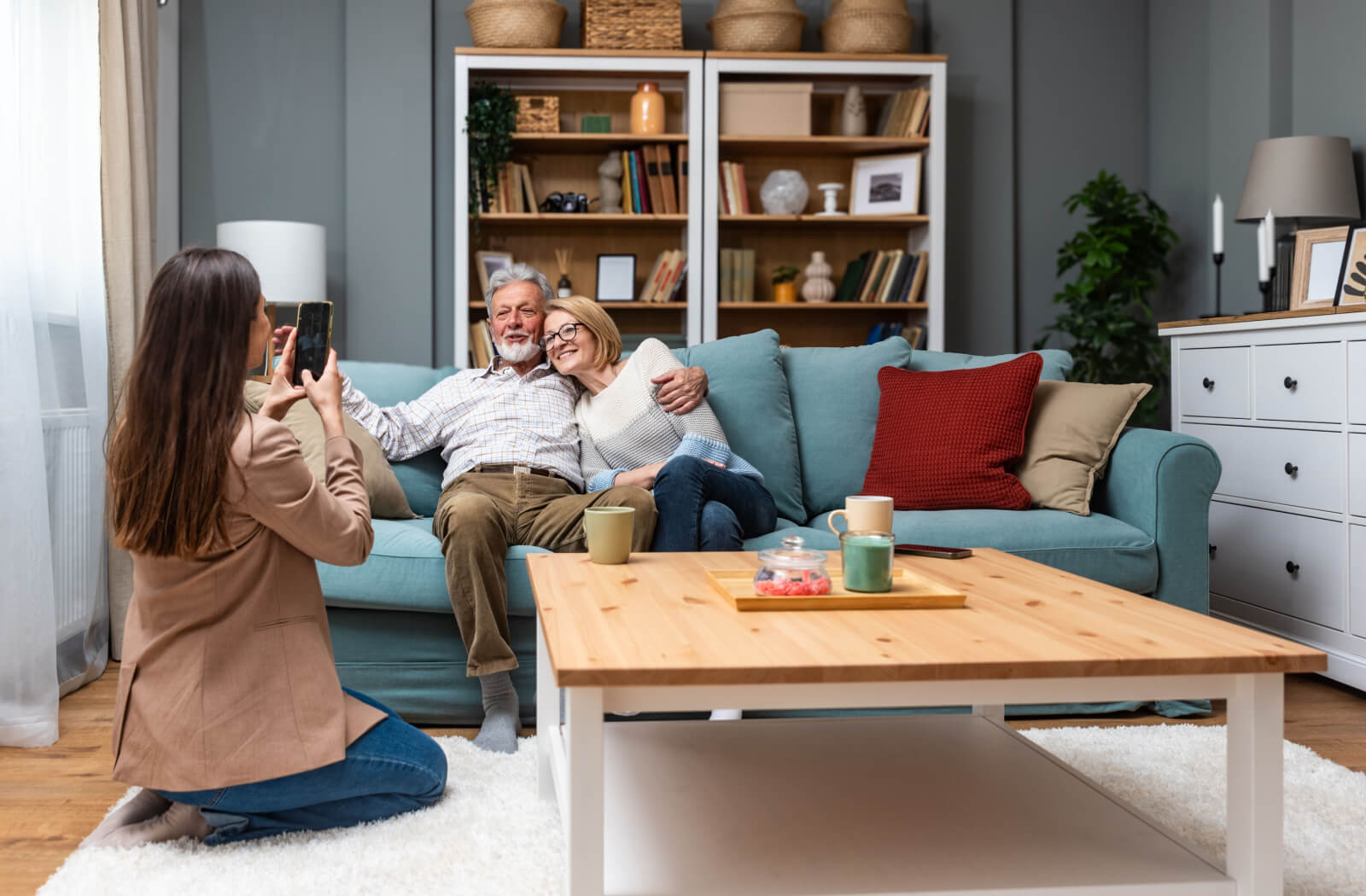 An adult visiting their parents in senior living, kneeling on the carpet to take a picture on their phone.