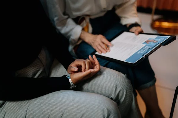 Two employee are sitting. One person is holding a clipboard with a resume discussing how to write a resume for fresh grads