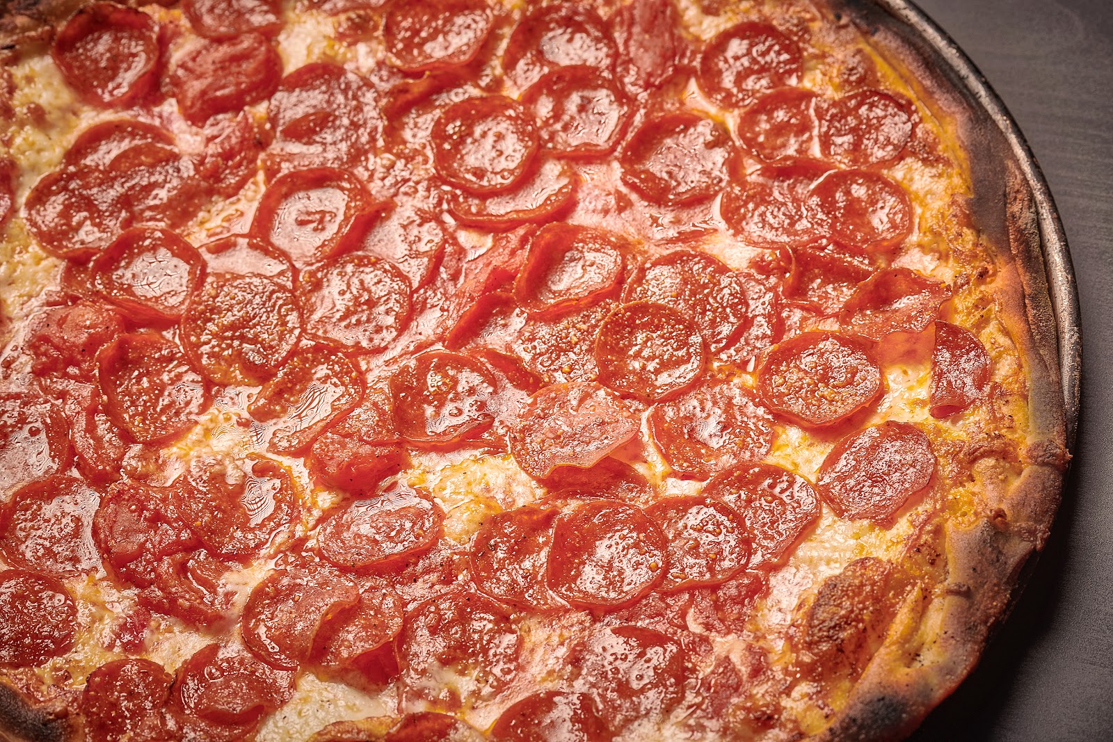 A crispy, golden-brown pepperoni pizza with melted cheese and perfectly charred edges, served on a dark pan with glistening pepperoni slices.