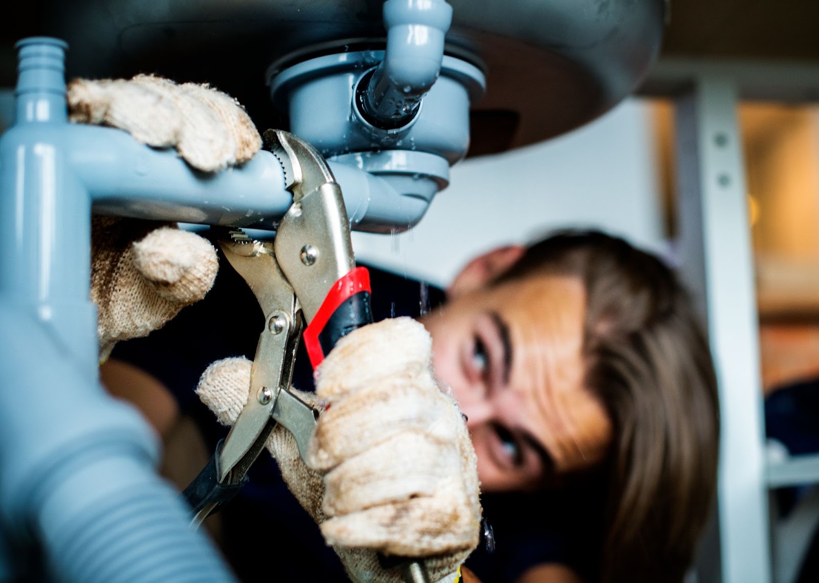 A close-up of a man repairing a kitchen sink as part of plumbing repairs.