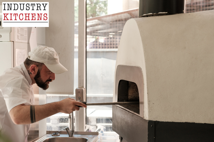 Professional baker tending to a wood-fired oven with proper tools, demonstrating maintenance techniques