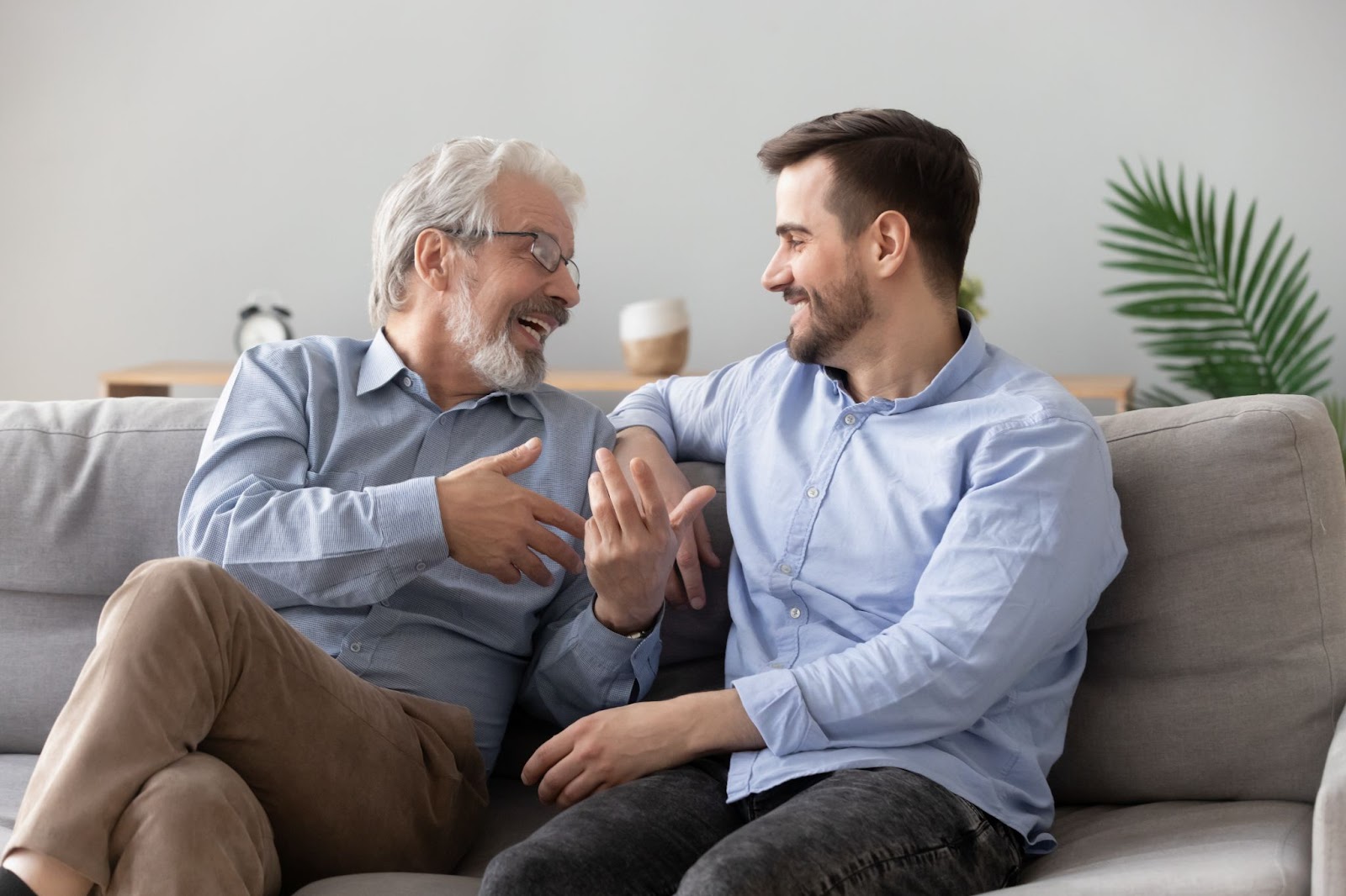 Two men are sitting on a couch, smiling and engaging in a relaxed conversation.