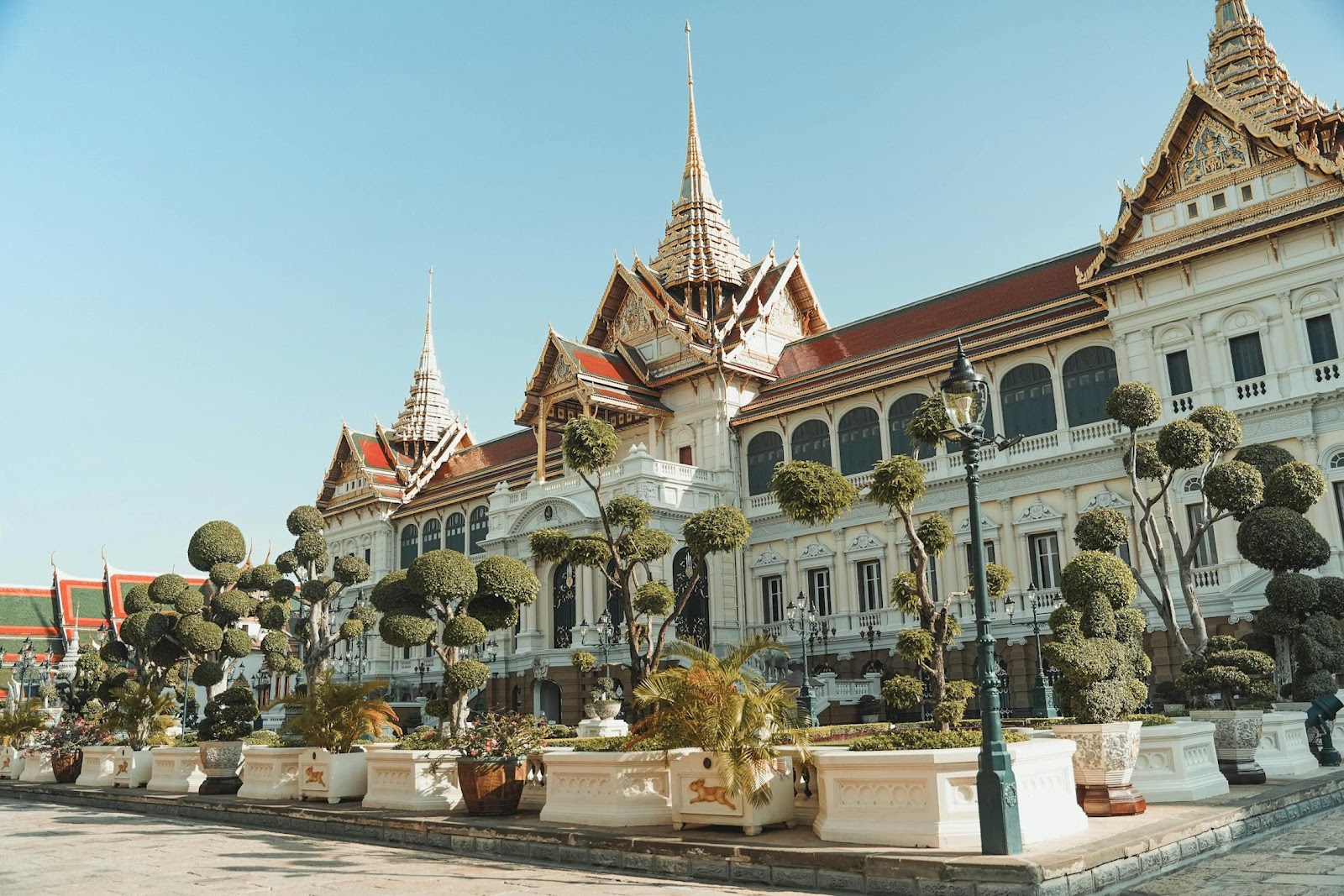 A large white building with a red roof with Grand Palace in the background

Description automatically generated