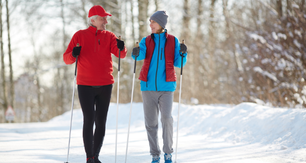 Senior couple taking a walk in the snow with walking sticks