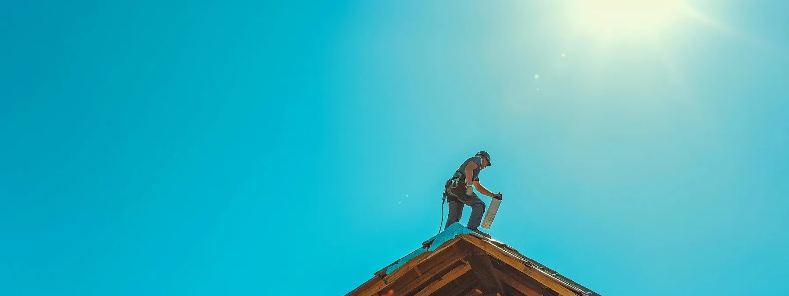 a person standing on a ladder with a tube of sealant in hand, repairing a roof under a clear blue sky.