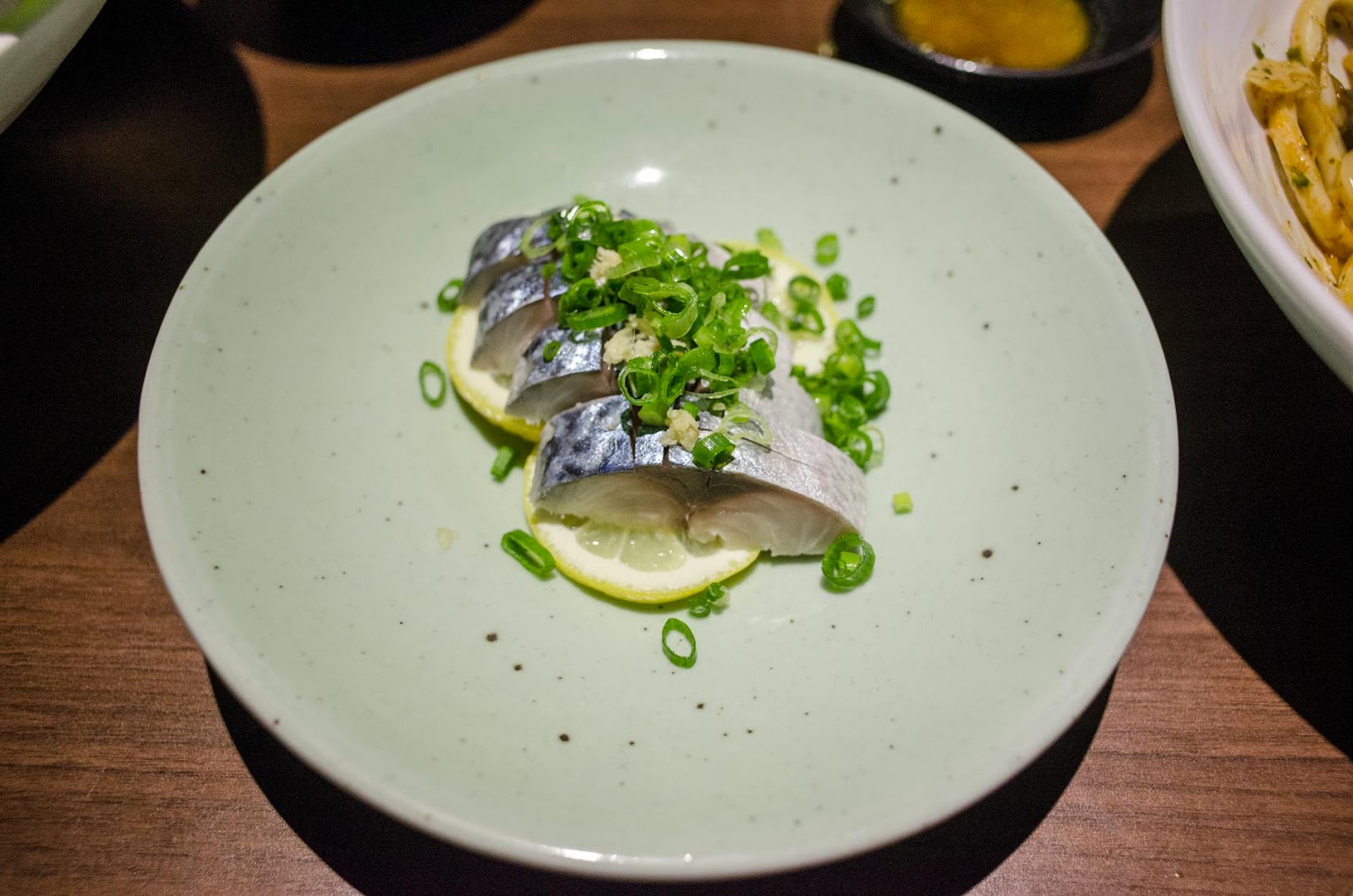 Close-up of nigiri sushi with fish, lemon slices, and green onions on a ceramic plate.