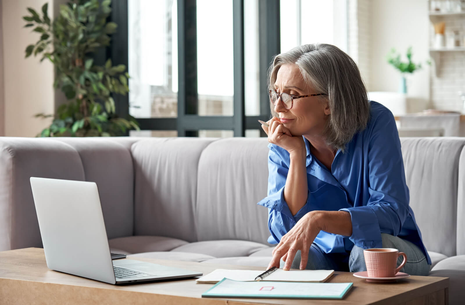 An older adult on their couch with a laptop and several notebooks, thinking of new passwords to safely stay online.