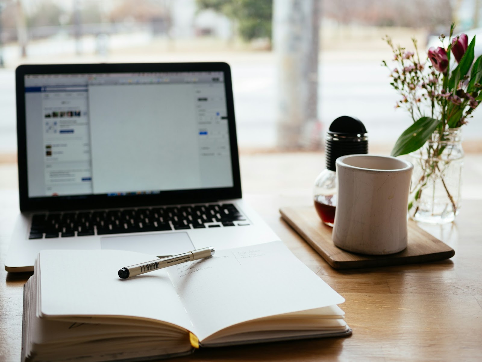 An image of a laptop in a desk with a notebook and a pen