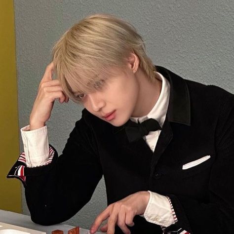 This containTaemin in a tuxedo is sitting at a table and looking down