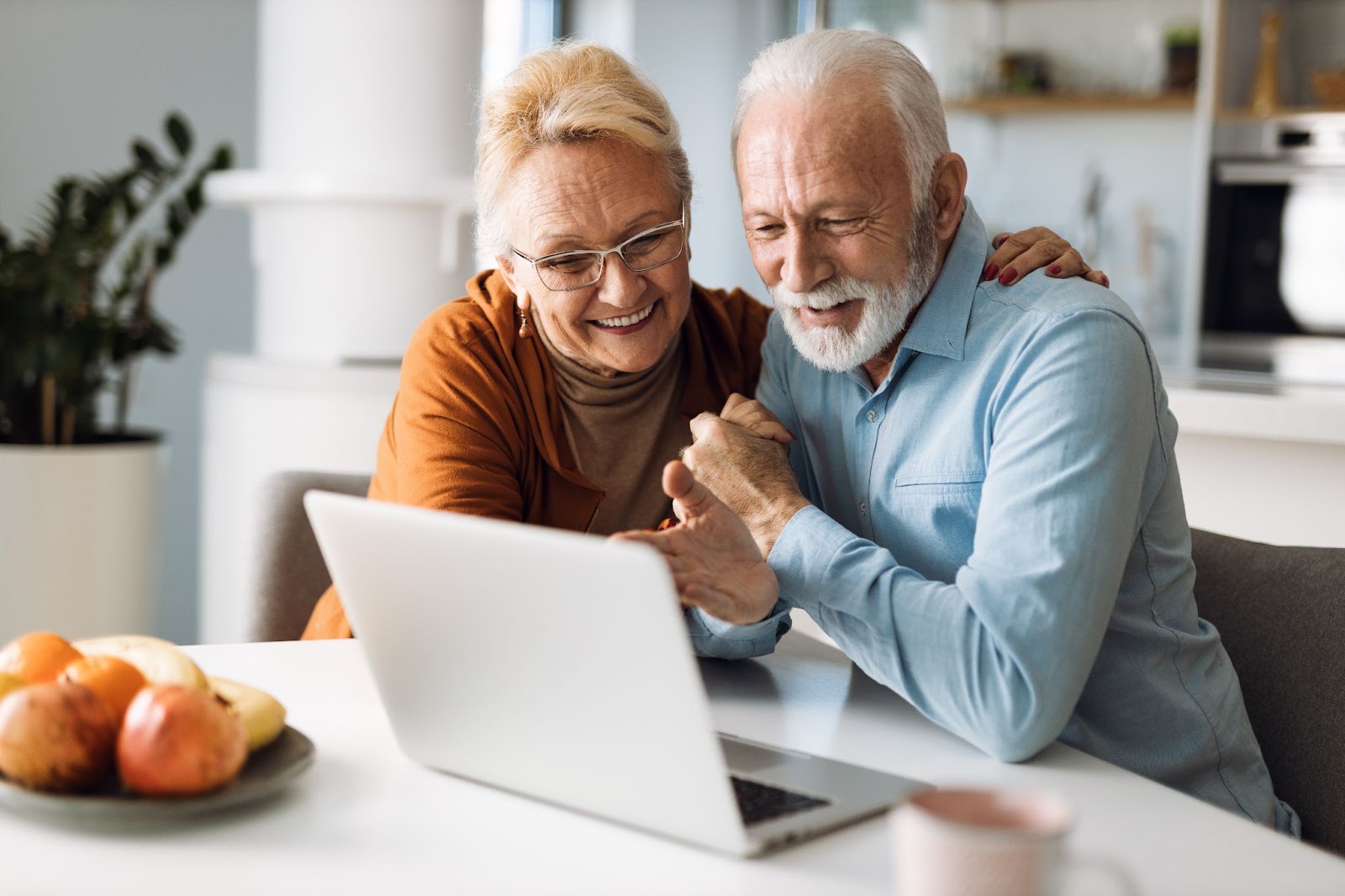 A senior couple smiling and hugging while researching retirement communities.