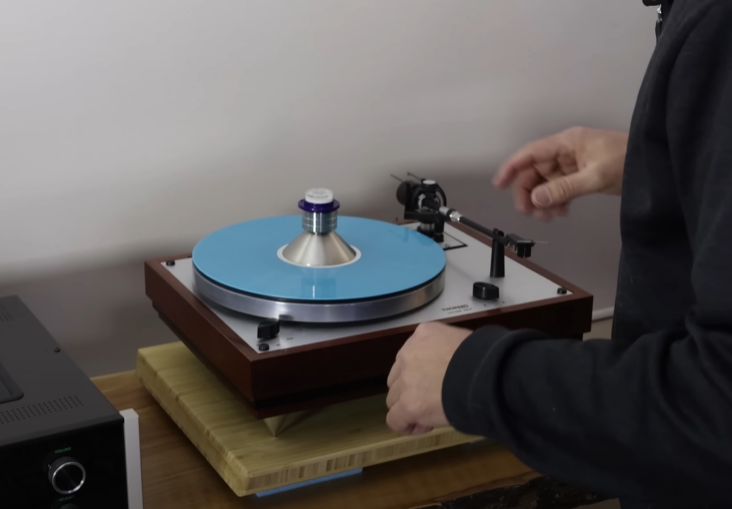 A person setting up a turntable with a blue vinyl and a silver record weight.